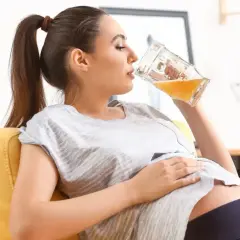 Kobieta w ciąży relaksuje się na kanapie, pijąc piwo bezalkoholowe.