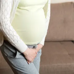 Kobieta w ciąży, z dłońmi przytrzymującymi brzuch, martwi się zielonym śluzem.