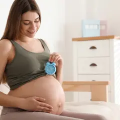 Uśmiechnięta kobieta w 9 miesiącu ciąży trzyma niebieski budzik na brzuchu. Czas na poród!