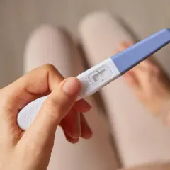 Dłoń trzyma test ciążowy z dwoma wyraźnymi kreskami, sugerującymi wczesną, 3-dniową ciążę.
