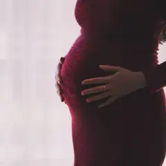 Ciężarna kobieta w czerwonej sukience obejmuje brzuch. Dylematy związane z umową zlecenie a ciążą.