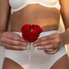 Kobieta w białej bieliźnie trzyma kubeczek menstruacyjny z czerwoną różą. Symbolizuje to nowy początek i powrót do równowagi po porodzie.