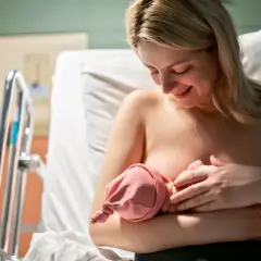 Uśmiechnięta mama karmi piersią noworodka. Pierwsze krople siary z piersi to cenny początek dla maluszka.