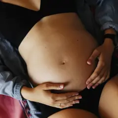 Brzuch kobiety w ciąży, dłonie delikatnie go obejmują. Może to być związane z bólem pachwin w ciąży.