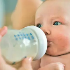 Niemowlę pije mleko z butelki. Rodzice często szukają informacji, ile powinno jeść niemowlę, tabela może pomóc.