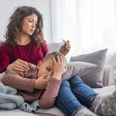 Zmartwiona mama mierzy gorączkę choremu dziecku, które ma zatkany nos. To mogą być **mykoplazma objawy**.