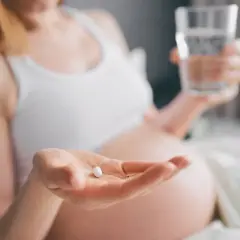 Ciężarna kobieta bierze tabletkę, by złagodzić objawy anginy. Dba o zdrowie swoje i dziecka.