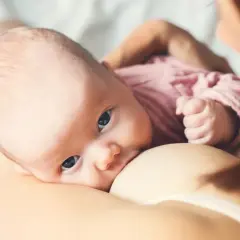 Niemowlę z niebieskimi oczami karmione piersią. To piękny przykład karmienia mieszanego, gdy mama karmi swoje dziecko.