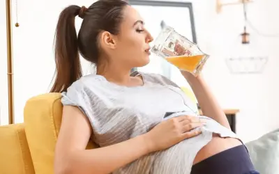 Kobieta w ciąży relaksuje się na kanapie, pijąc piwo bezalkoholowe.