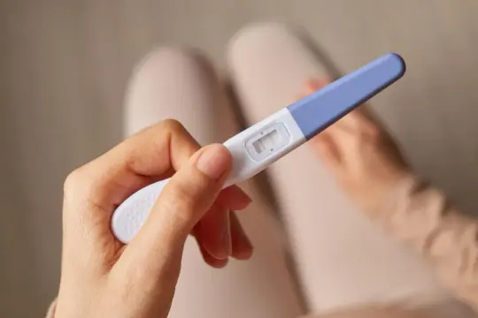 Dłoń trzyma test ciążowy z dwoma wyraźnymi kreskami, sugerującymi wczesną, 3-dniową ciążę.
