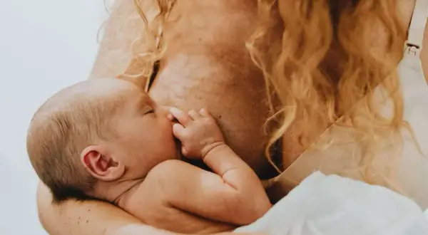 Ciepłe chwile karmienia piersią. Malutkie rączki otulają twarz dziecka, które śpi wtulone w mamę.