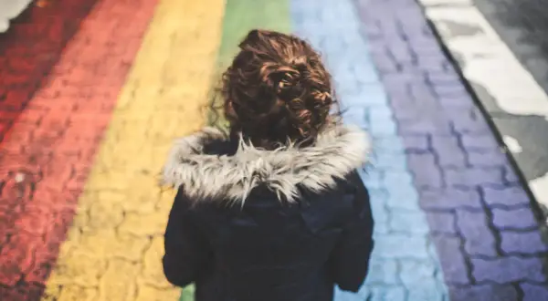 Dziecko z kręconymi włosami idzie po tęczowym przejściu dla pieszych.