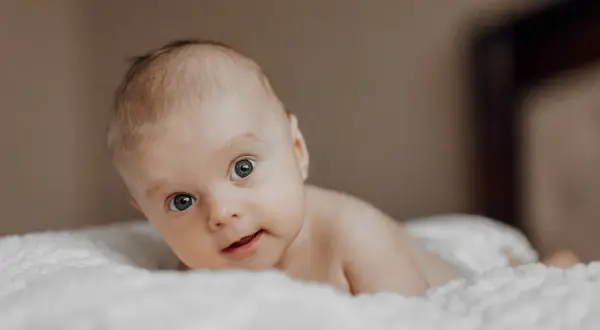 Niemowlę z niebieskimi oczami leży na białym kocyku. Jego wzrok jest skupiony, a usta lekko rozchylone. Zez u niemowlaka jest widoczny, ale nie przeszkadza mu w eksplorowaniu świata.