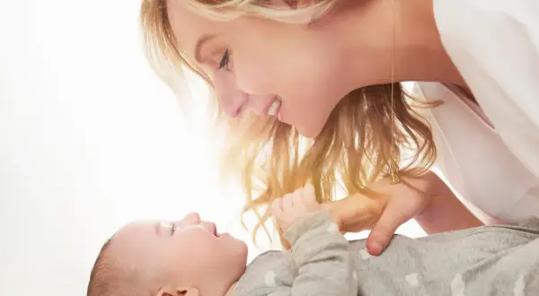 Uśmiechnięta mama pochyla się nad dzieckiem, które ma czkawkę u noworodka.