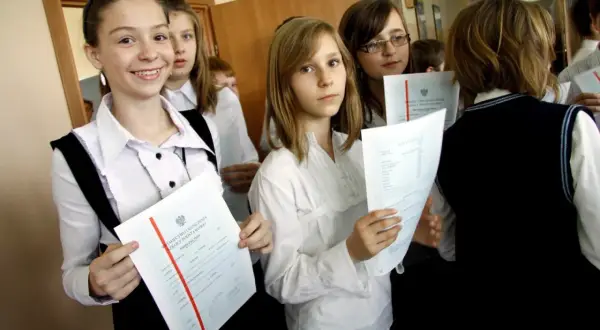 Uczennice z dumą trzymają świadectwa ukończenia szkoły. Na jednym z nich widoczny jest czerwony pasek średnia.