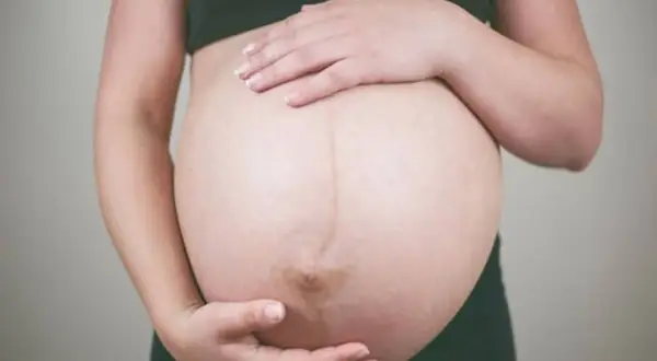 Dłońmi obejmuje ciążowy brzuch, wyczekując momentu, kiedy czuć ruchy dziecka.