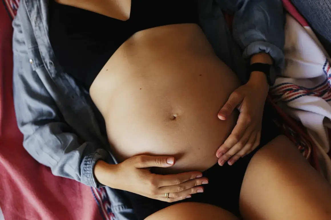 Brzuch kobiety w ciąży, dłonie delikatnie go obejmują. Może to być związane z bólem pachwin w ciąży.