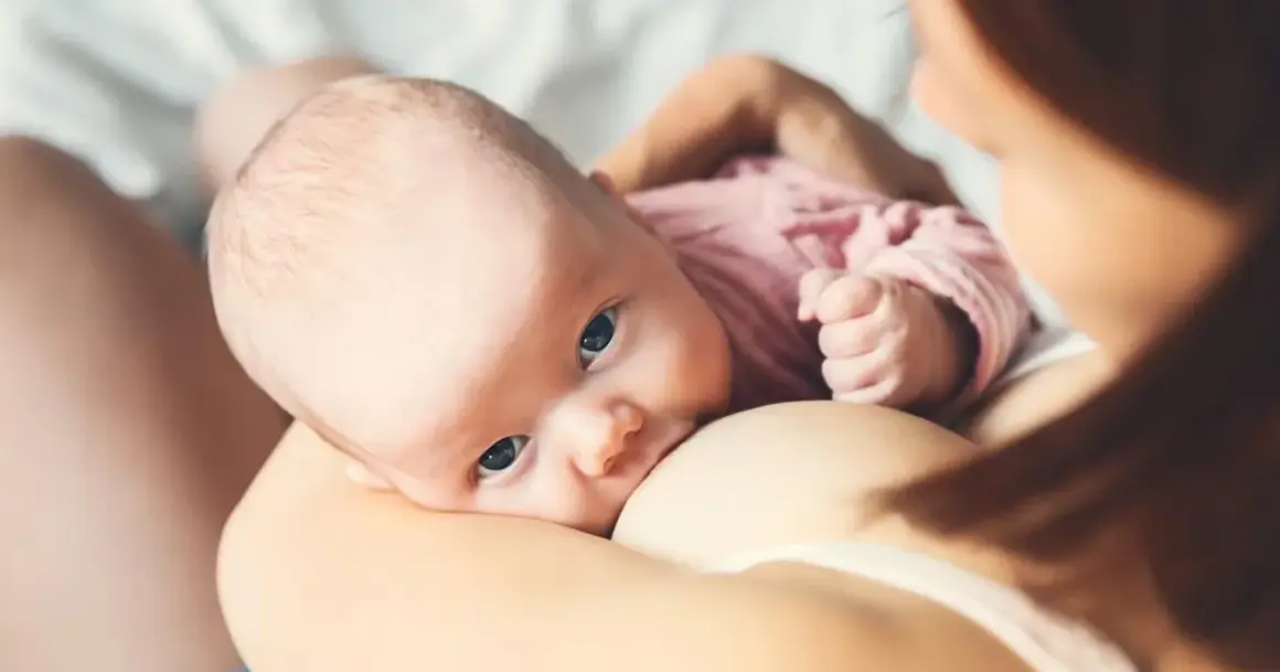 Niemowlę z niebieskimi oczami karmione piersią. To piękny przykład karmienia mieszanego, gdy mama karmi swoje dziecko.