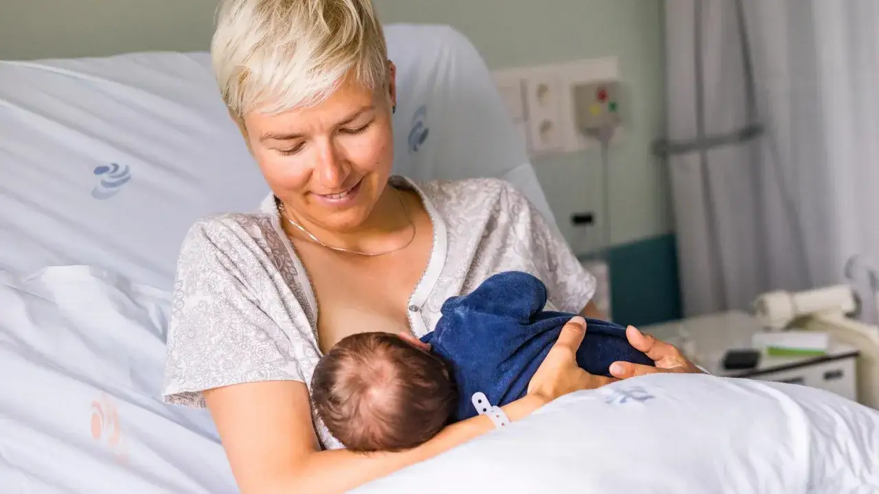 Uśmiechnięta mama karmi piersią noworodka. Pierwsze krople siary z piersi to cenny początek dla maluszka.